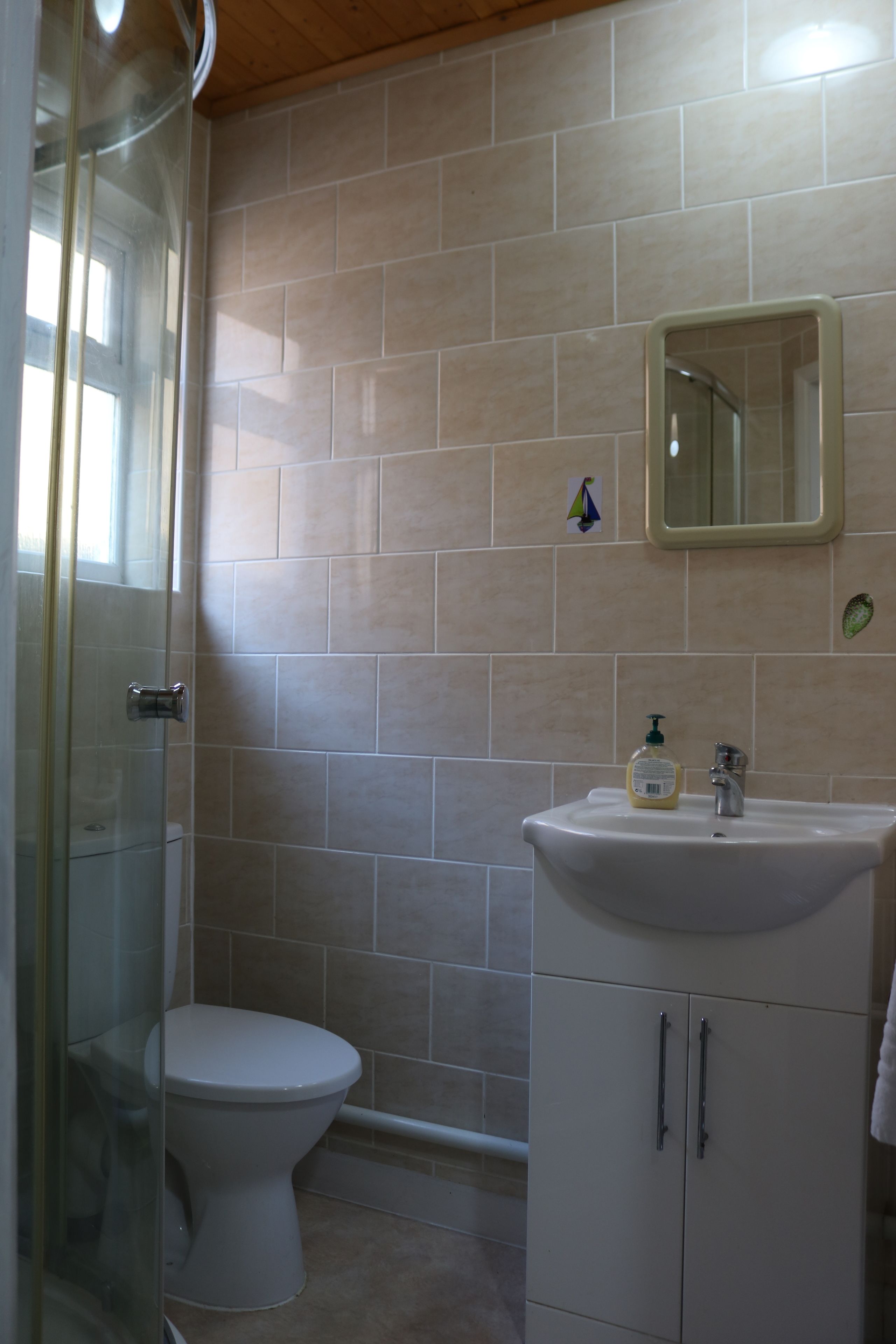 A bathroom with a glass shower enclosure, a toilet, a sink with a mirror, and beige tiled walls.