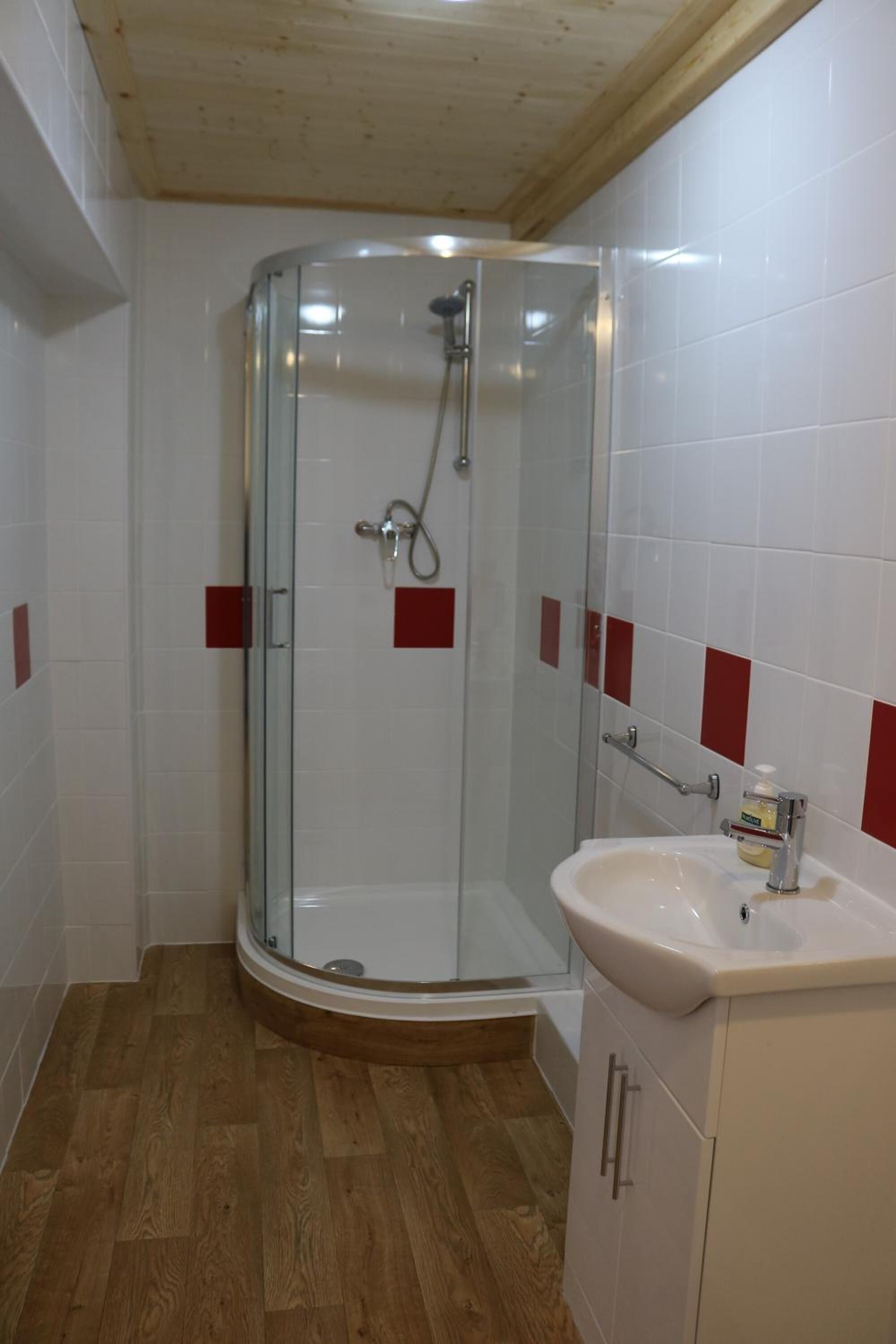 Una dutxa amb portes de vidre, un lavabo blanc i un paviment de fusta.