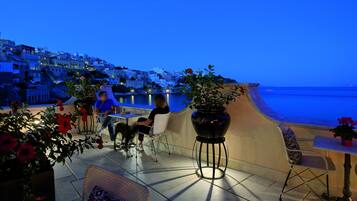 Una terraza con asientos al aire libre, vista al mar y una colina en el fondo.