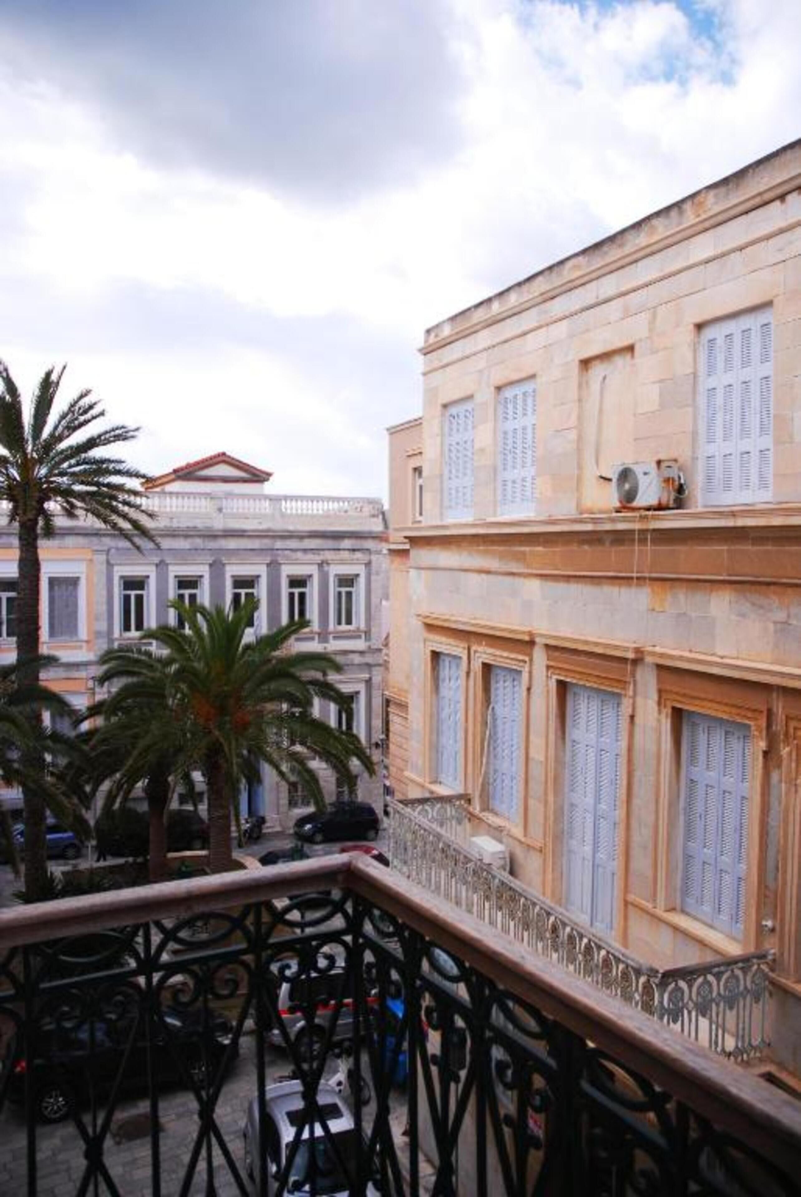 A balcony with a wrought iron railing, overlooking a street with parked cars and palm trees.