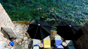 Una piscina de pedra amb aigua cristal·lina, envoltada de gandules i ombrelles.