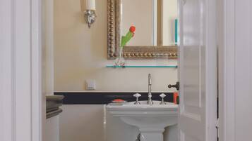 Um banheiro com pia branca, espelho com moldura decorativa, um banquinho pequeno e piso xadrez.