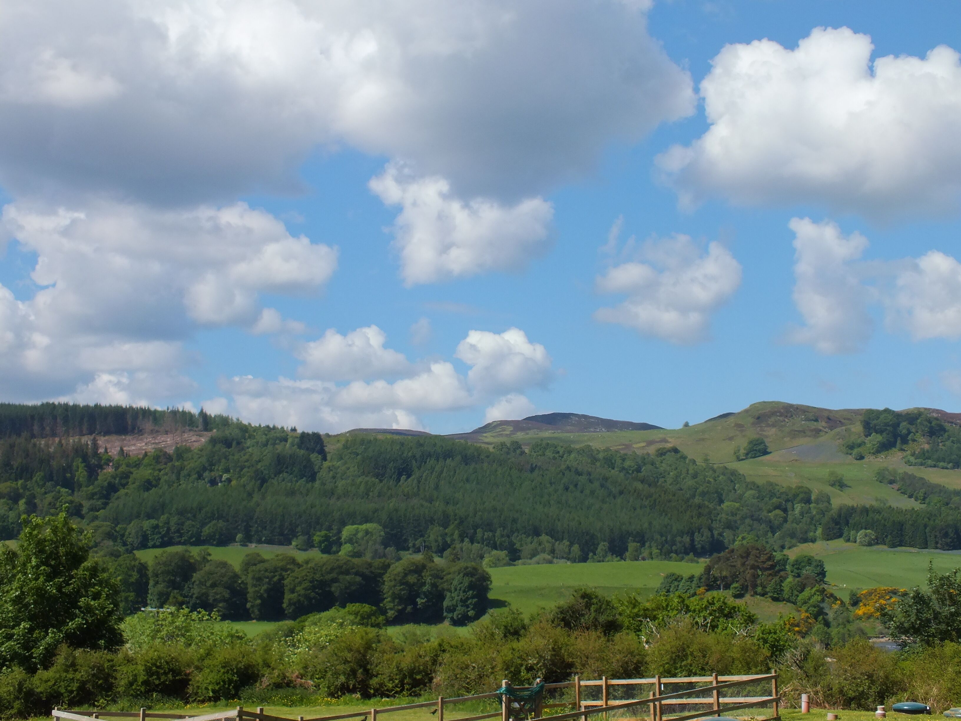 A scenic view of a hilly landscape with a wooden fence in the foreground, likely indicating a park or natural area.