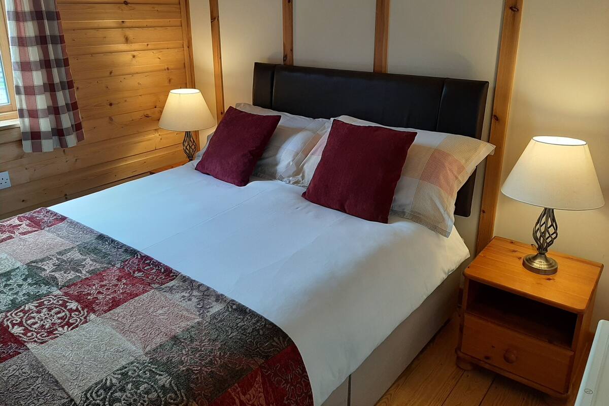 Una cama bien hecha con un edredón estampado, dos almohadas y dos lámparas de noche sobre mesitas de madera.