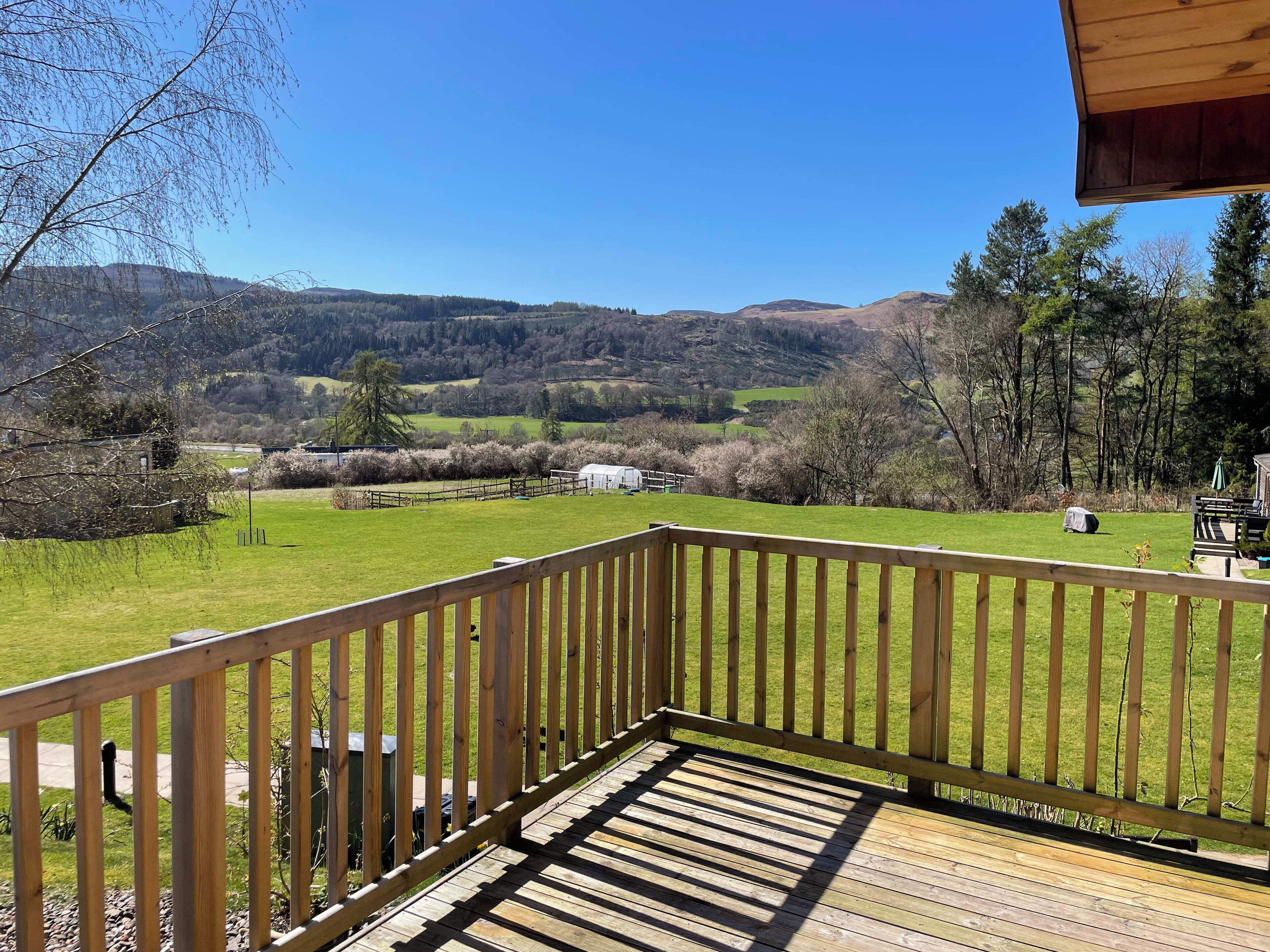 A wooden deck with a view of a green field and distant hills.