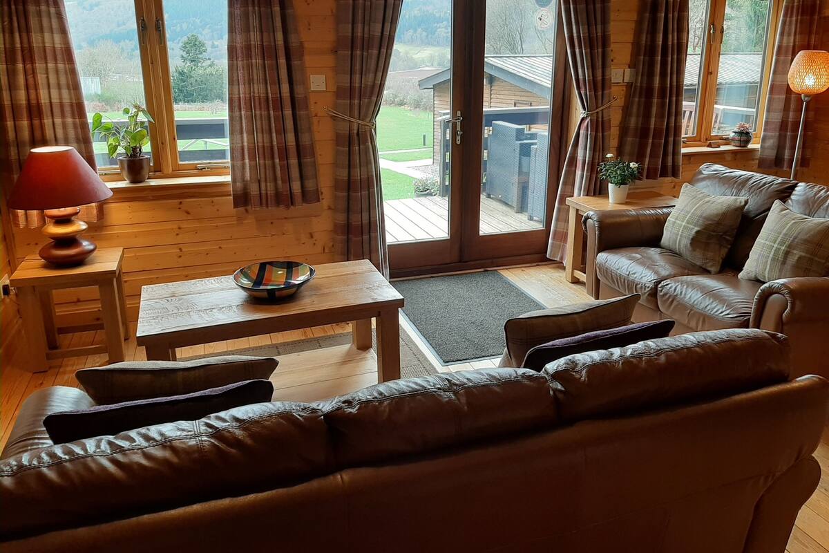 Una habitación acogedora con un sofá de cuero, una mesa de madera y vistas a una cabaña de madera a través de una puerta de cristal.