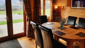 A wooden interior with a dining table, chairs, a vase with flowers, and a framed picture on the wall. - Tayview Lodges (Pitlochry)