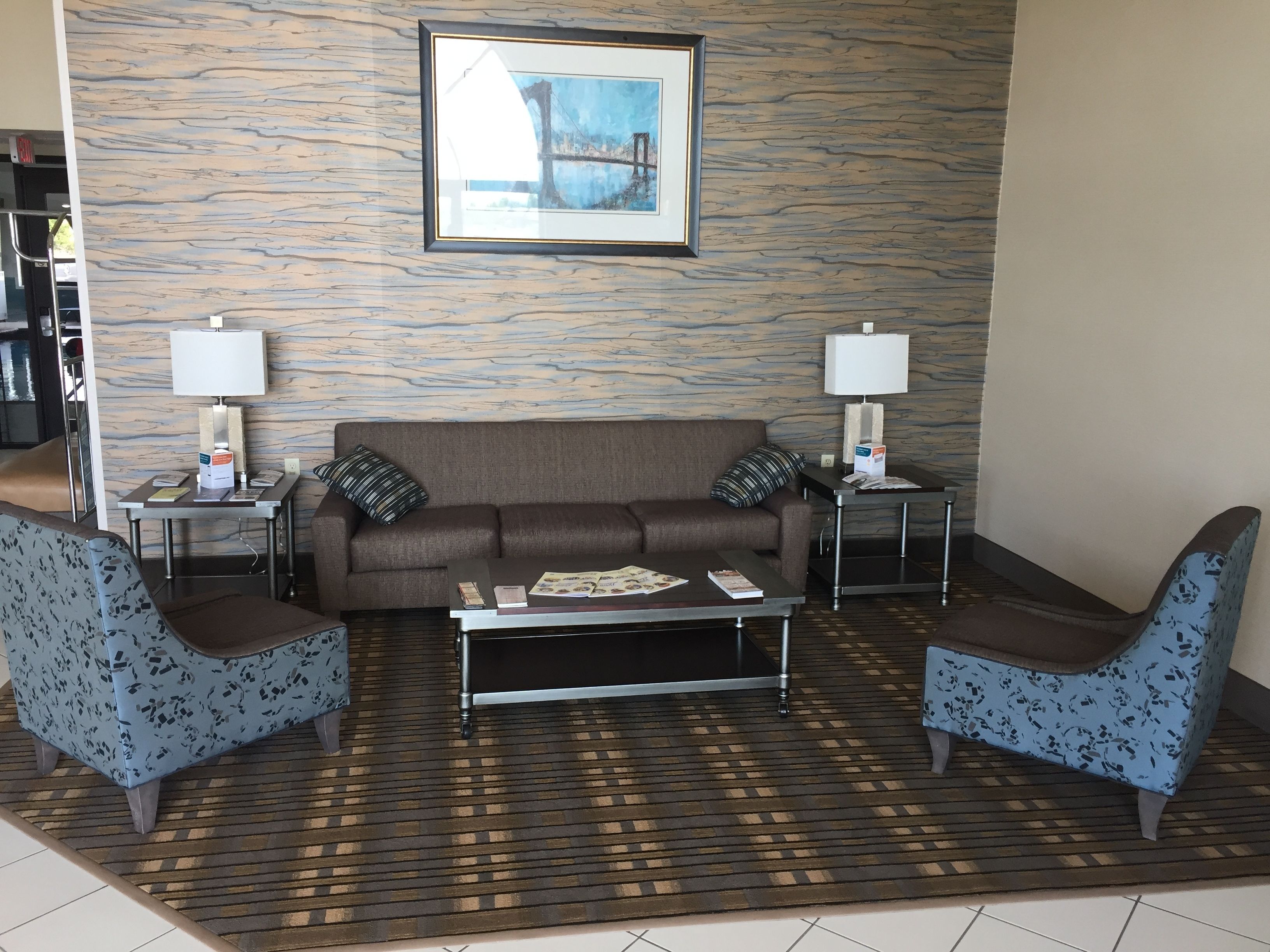 A modern living room with a brown sofa, two patterned armchairs, a coffee table, and two side tables with lamps. A framed picture hangs above the sofa.