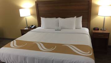 Une chambre d’hôtel avec un grand lit, deux tables de chevet, une petite table, une lampe, un téléphone et une horloge numérique.