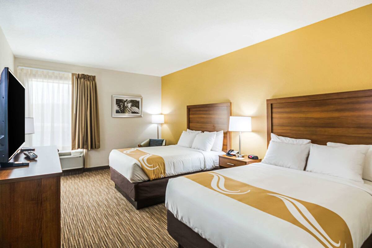 Habitación de hotel con dos camas, un escritorio, un televisor y una ventana con cortinas.