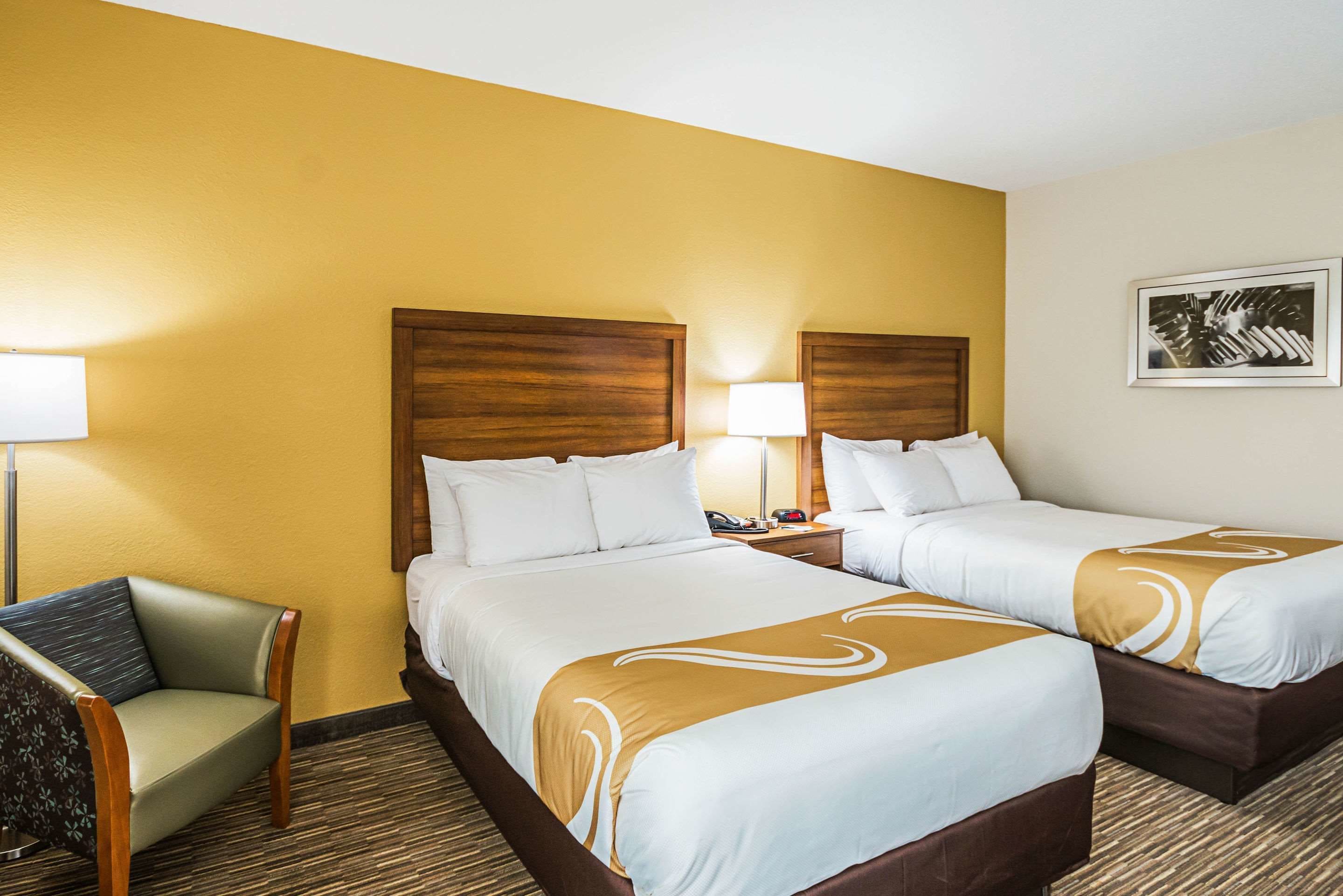 A hotel room with two beds, a chair, and a lamp.