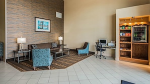 Un vestíbulo de hotel con pared de piedra, un cuadro enmarcado, una zona de estar con sofá y sillas, un escritorio con computadora y un bar de aperitivos.