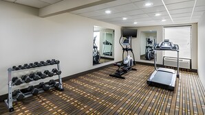 Un gimnasio con equipo de ejercicio, un espejo grande y piso de madera.