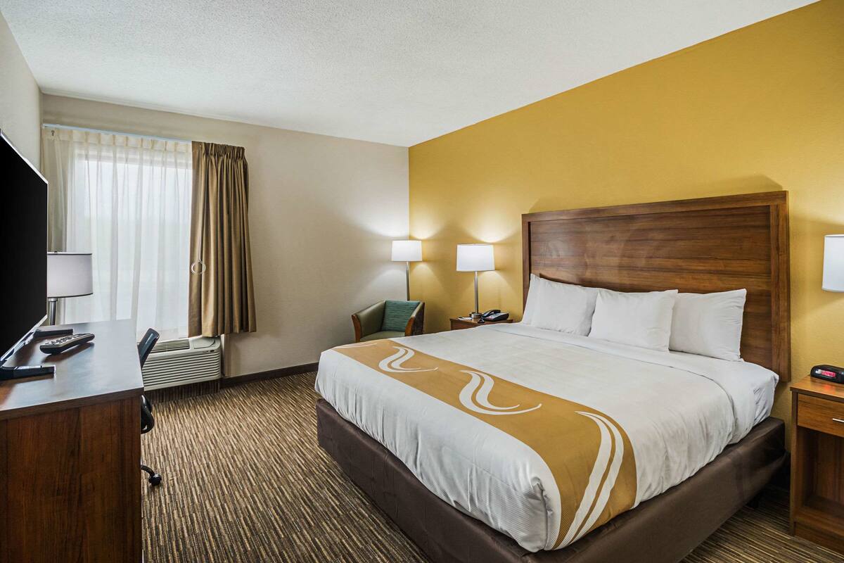 Una habitación de hotel con una cama grande, un escritorio con teléfono y una televisión.