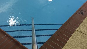 A swimming pool with clear water, a metal ladder, and tiled edges.