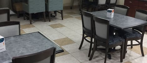 Habitación de hotel con mostrador de recepción, zona de estar con mesas y sillas, televisor de pantalla plana montado en la pared y piso de baldosas.