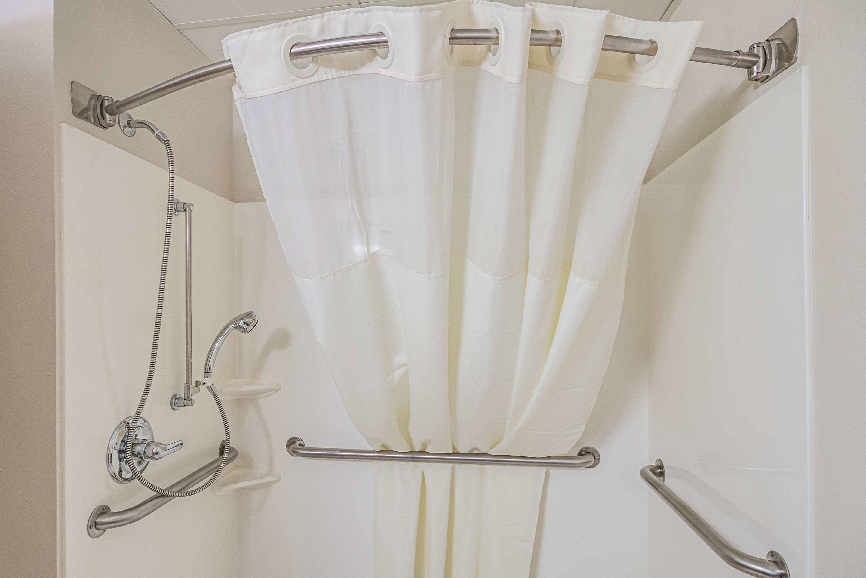 A shower area with a white curtain, a handheld showerhead, and a grab bar.