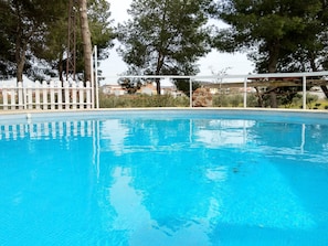 Una piscina blava i cristal·lina amb una tanca blanca i arbres al fons.