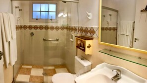 Un baño con cabina de ducha de vidrio, inodoro, lavabo y tocador con espejo.
