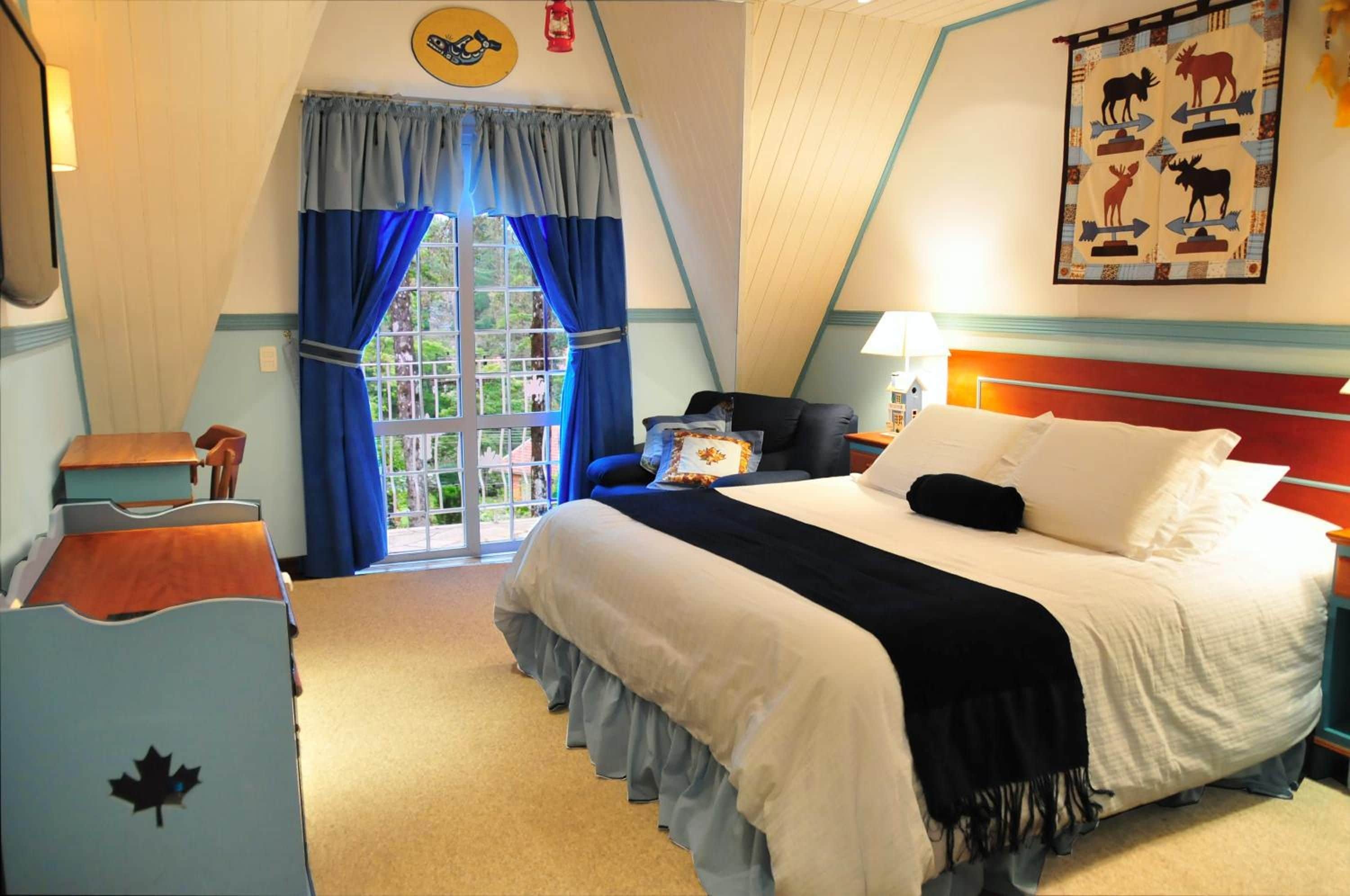 A hotel room with a bed, a desk, a chair, a window with curtains, and a wall with a wildlife-themed artwork.