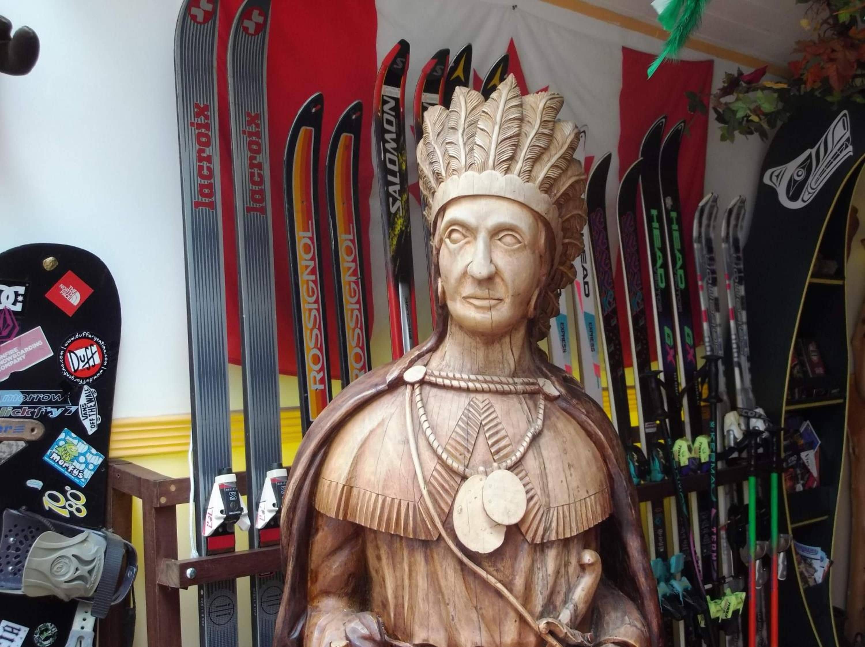 A wooden statue of a historical figure with a headdress, surrounded by skis.
