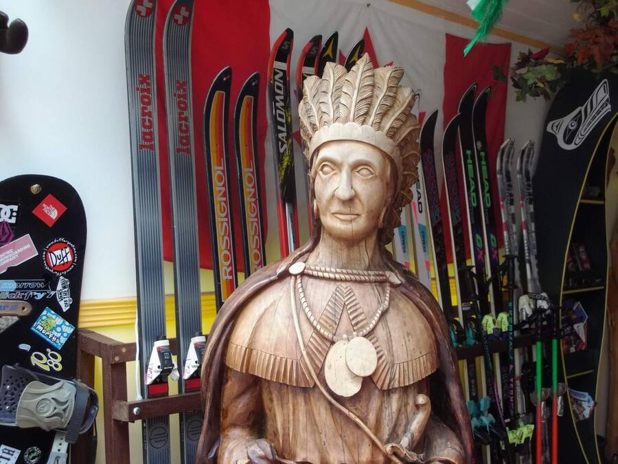 A wooden statue of a historical figure with a headdress, surrounded by skis.