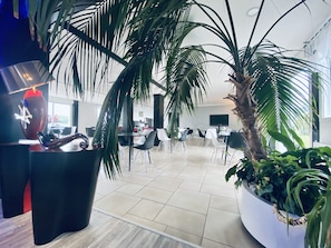 Un espace intérieur moderne, agrémenté d’un grand palmier en pot, de chaises noires et blanches, et d’un vase rouge au motif géométrique.