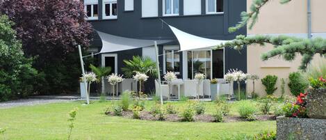 En toetages bygning med balkon, omgivet af en velplejet have med forskellige planter og blomster.