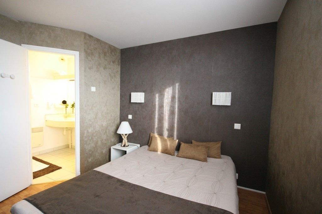 A bedroom with a bed, bedside table, lamp, and two wall-mounted light fixtures.