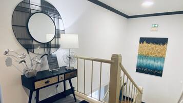 A hotel lobby with a black console table, a round mirror, a wall-mounted fan, and a painting.