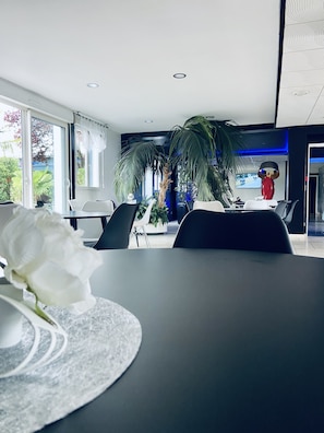 A modern dining area with a large table, chairs, and a potted plant. - Hôtel Air-Lane (Saint-Leger-sous-Brienne)
