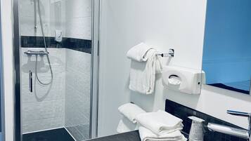 A modern bathroom with a glass-enclosed shower, a white towel rack, a red bowl sink, and a blue accent wall.
