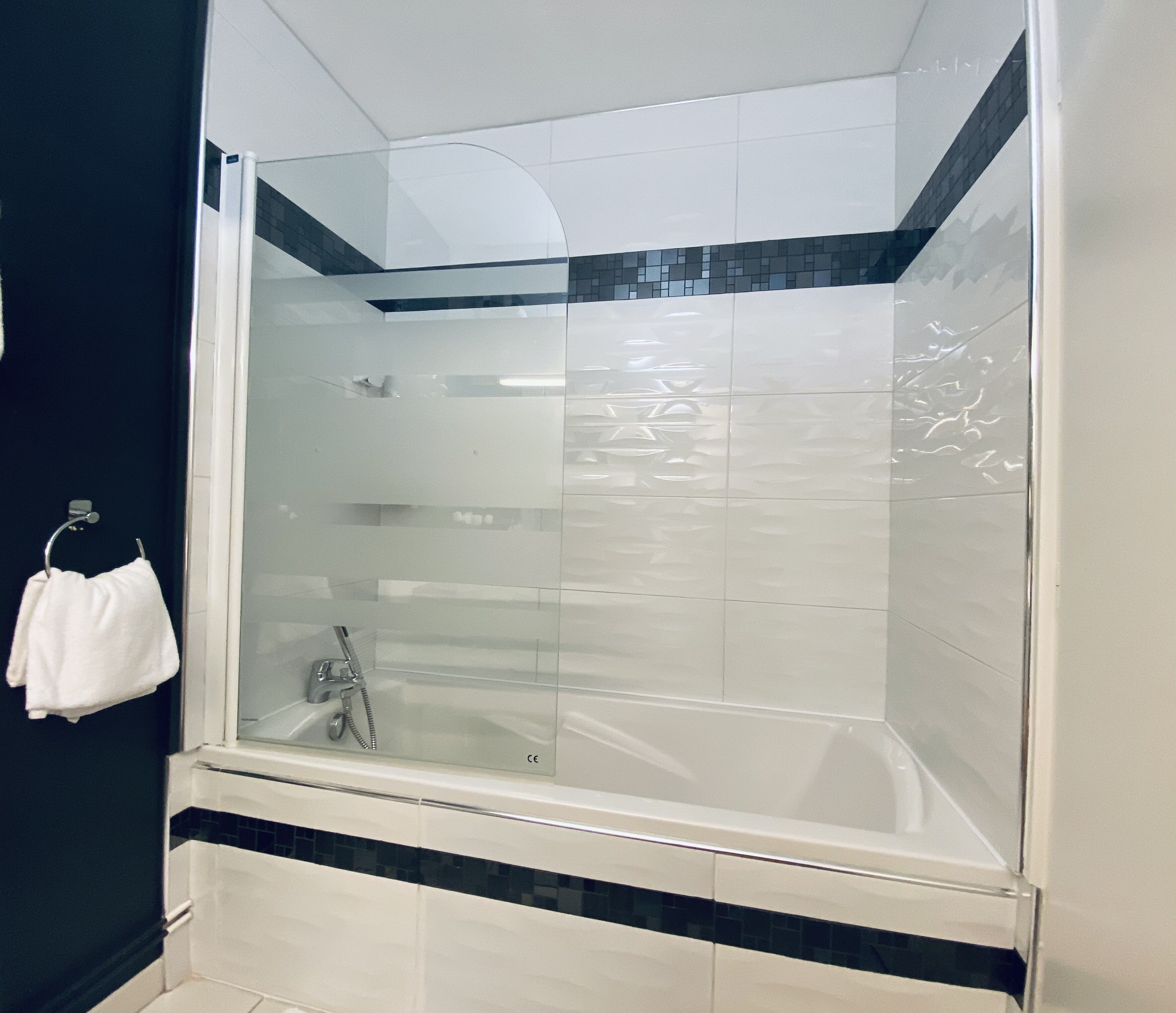 Un baño moderno con ducha envuelta en vidrio, azulejos blancos y una banda decorativa negra.