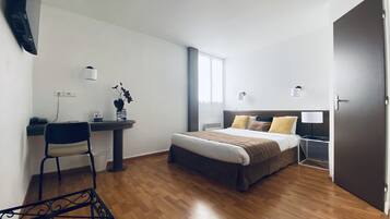 Habitación de hotel con una cama, un escritorio, una silla y una mesita con una planta.