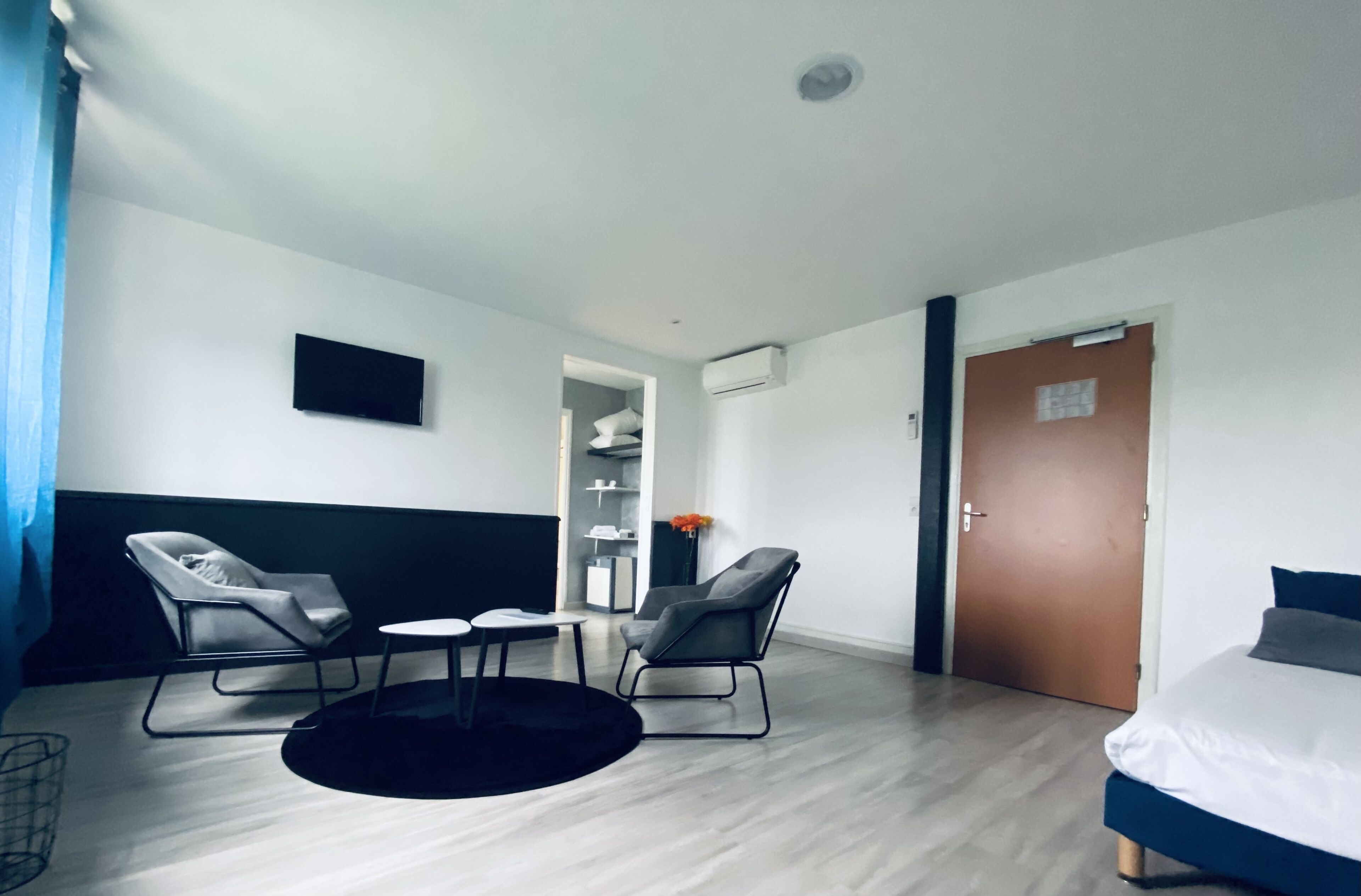 Ein modernes Hotelzimmer mit Bett, zwei Sessel, einem kleinen Tisch, einem Fernseher und einem Kleiderschrank.