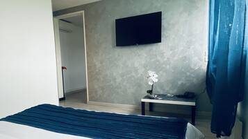 Quarto de hotel com cama, televisão de tela plana na parede, mesa pequena com um vaso de flores e cortina azul.