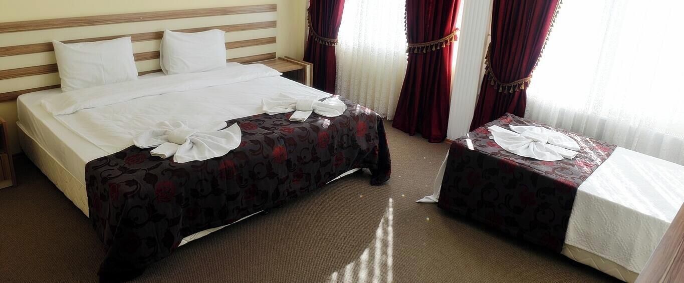 A hotel room with a bed, a bedside table, a small table, and a window with curtains.