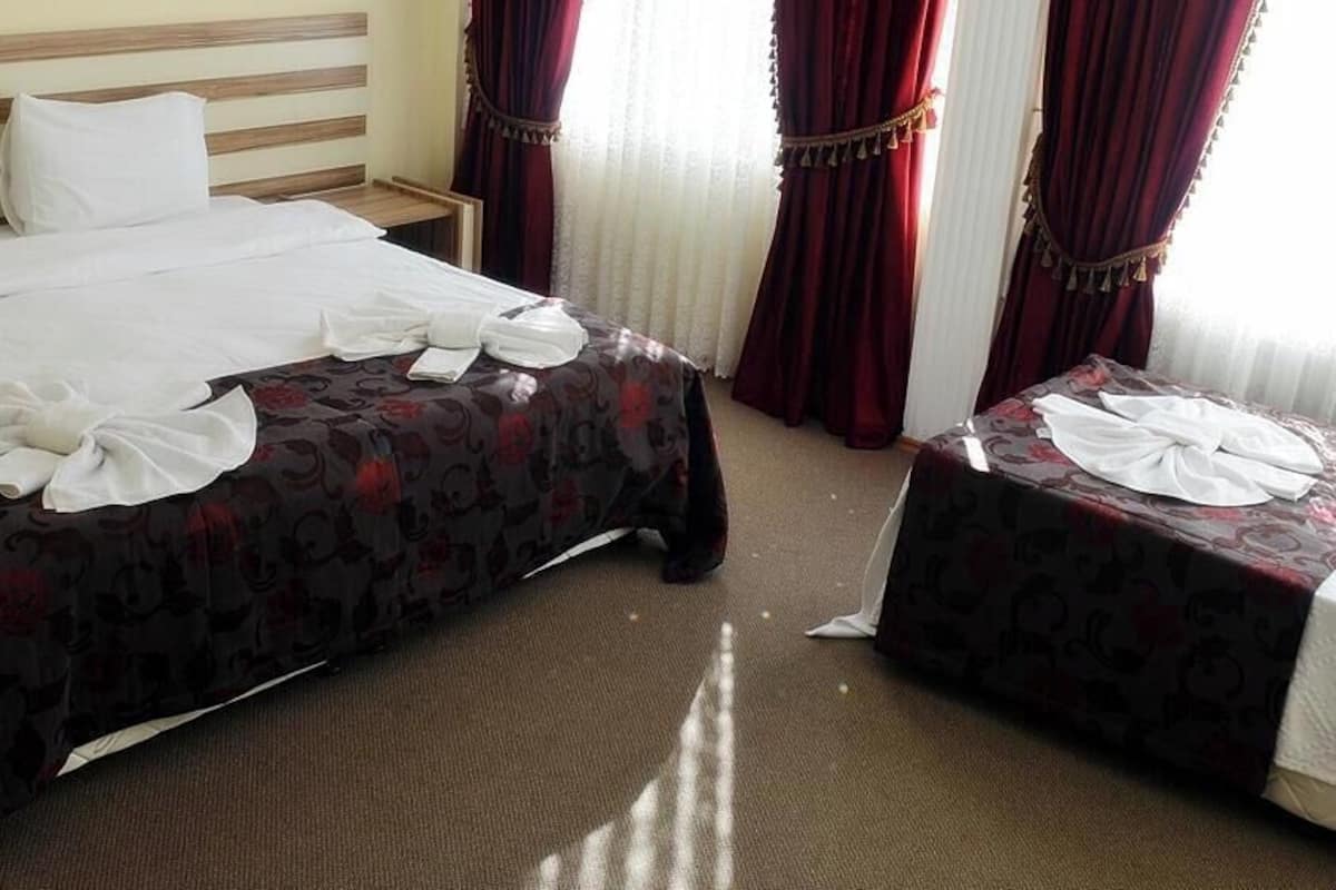 A hotel room with a bed, a bedside table, a small table, and a window with curtains.