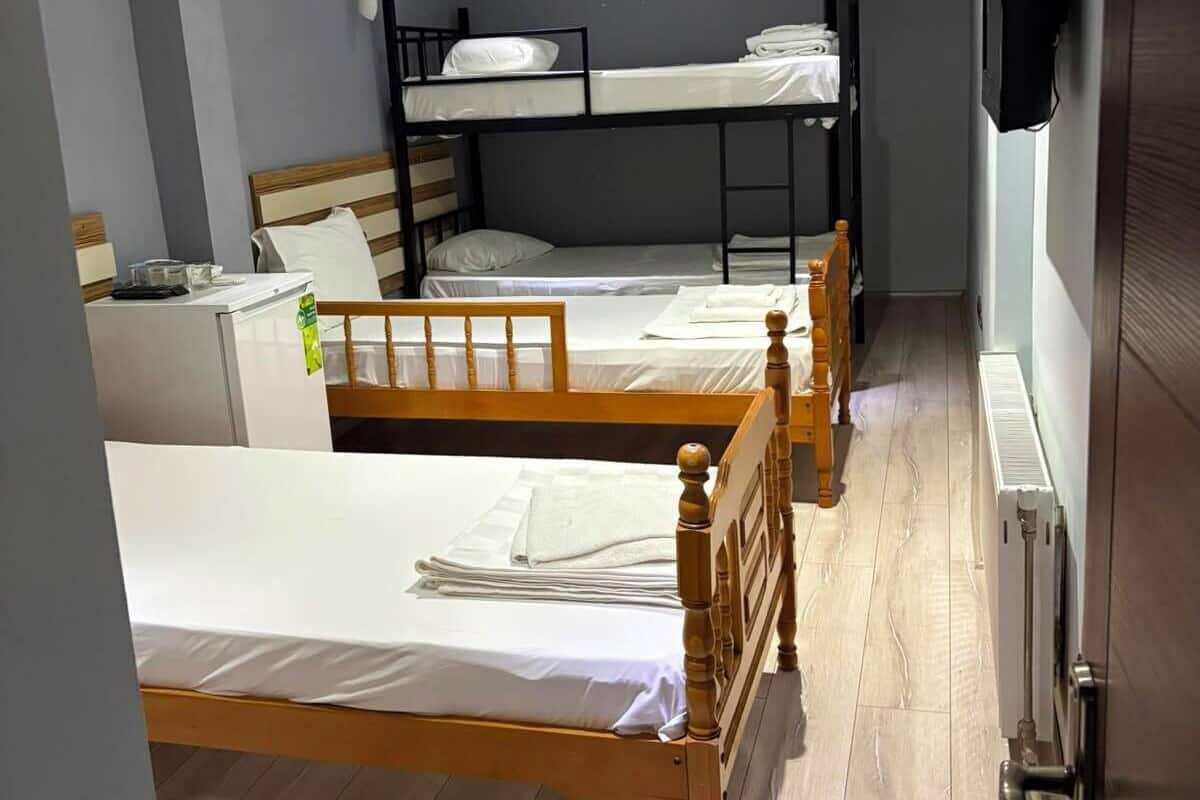 A room with bunk beds, a wooden floor, a radiator, and a television on the wall.