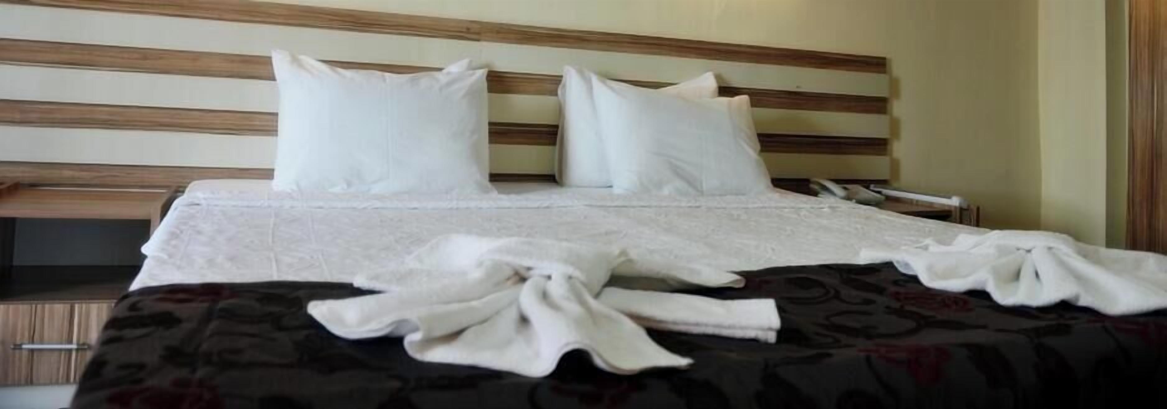 A neatly made bed with white linens and pillows, a wooden headboard, and a dark patterned bedspread.