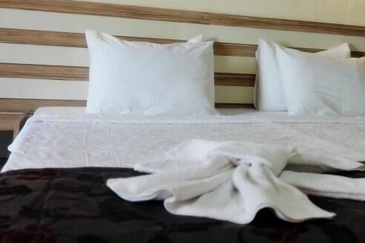 A neatly made bed with white linens and pillows, a wooden headboard, and a dark patterned bedspread.