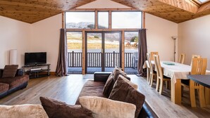 A spacious living area with a large window, wooden ceiling, and a dining area with a table and chairs. - Scottish Highland Lodge (Pitlochry)