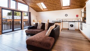 A spacious living area with a large sofa, a kitchen with a washing machine, and a balcony with a view. - Scottish Highland Lodge (Pitlochry)