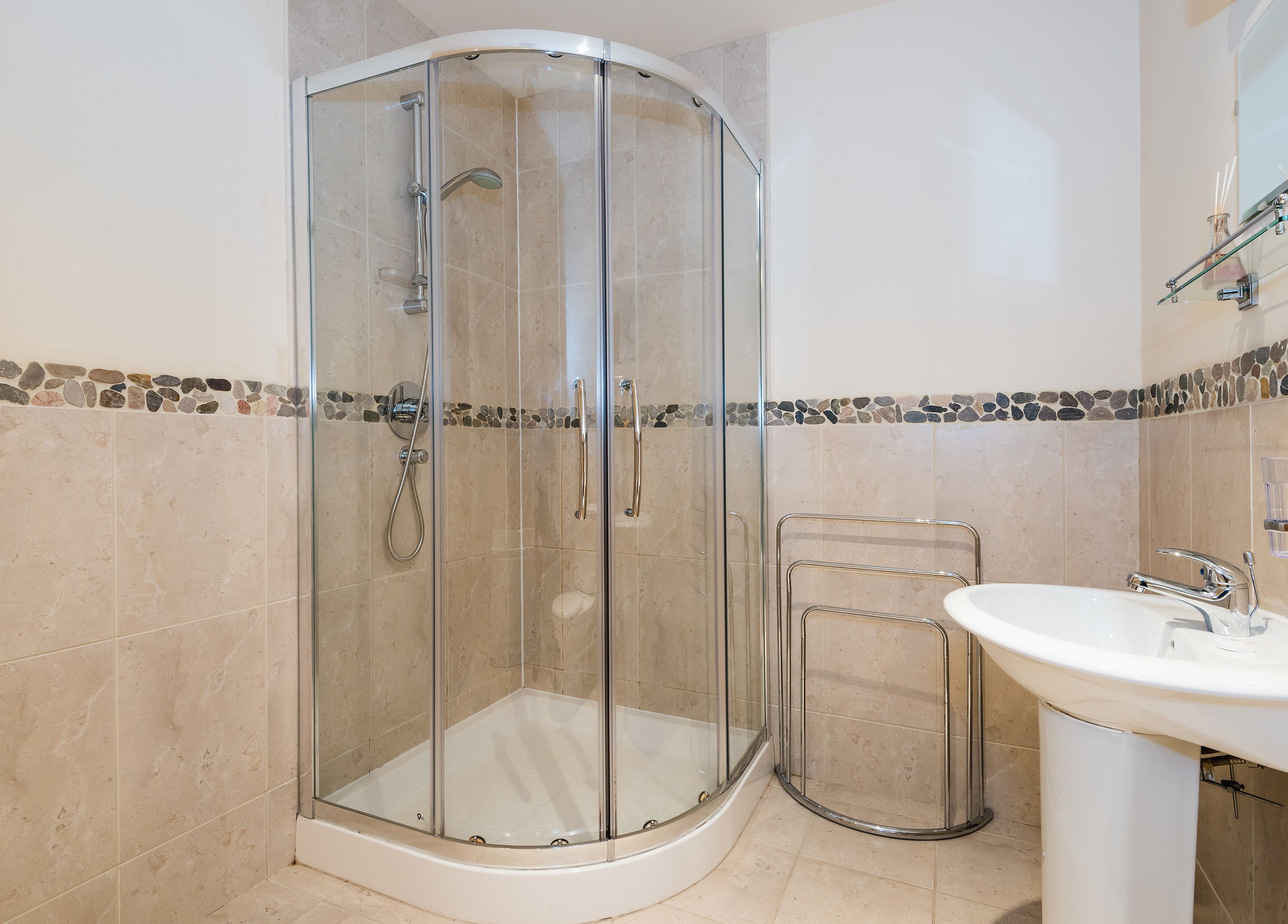 Un baño moderno con ducha de vidrio, lavamanos blanco y piso de baldosas.