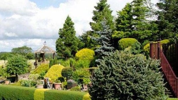 Um jardim bem cuidado, com sebes podadas, um gazebo e diversas árvores.