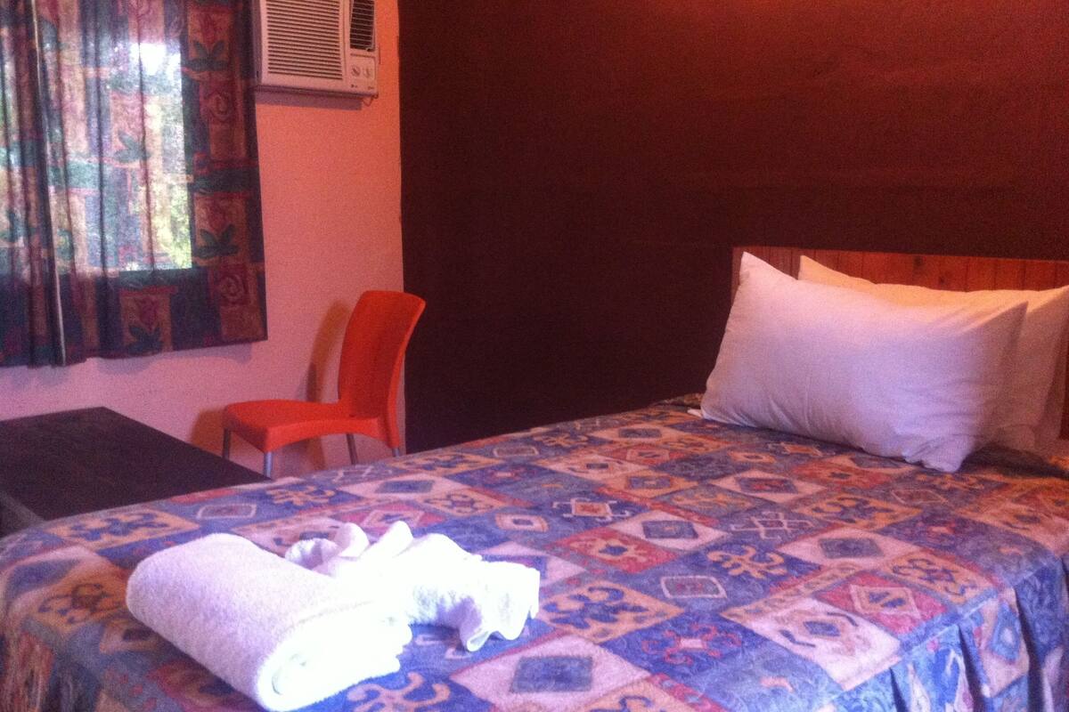 Una habitación de hotel con cama, una silla, una mesa y una ventana con cortinas.