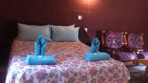 Een hotelkamer met een bed, twee handdoeken op het bed gevouwen, een bloemenprint bedspreidek en een stoel met een bloemenmotief.