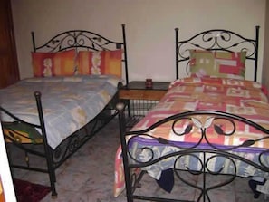 A room with two metal beds with ornate headboards, a small bedside table, and a wall-mounted shelf. - Riad Rahba (Marrakech)
