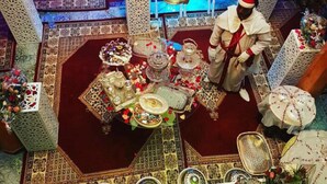 Un comedor tradicional con decoración elaborada, una araña y una persona con vestimenta ceremonial.