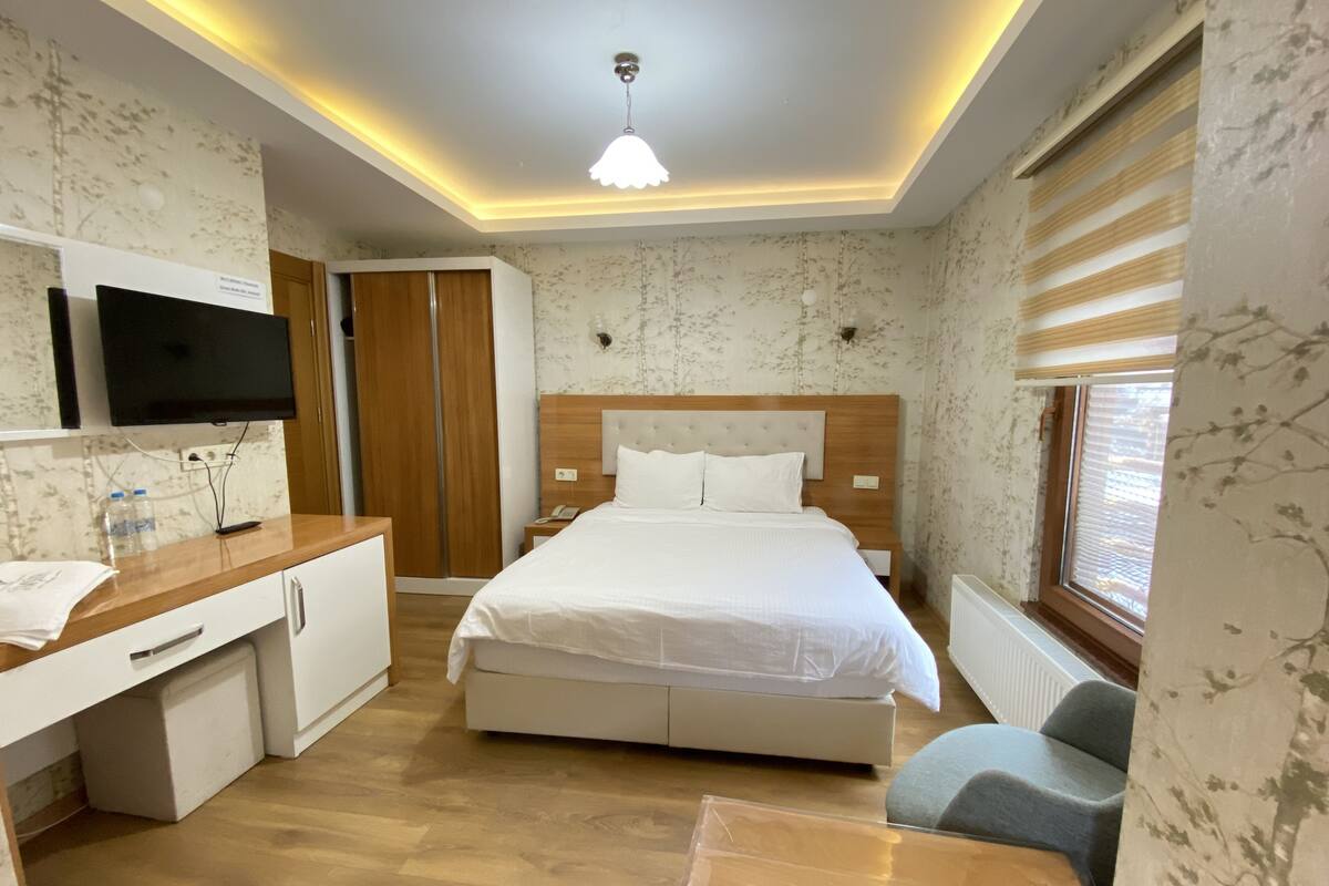 A hotel room with a bed, bedside table, wardrobe, and a television on the wall.